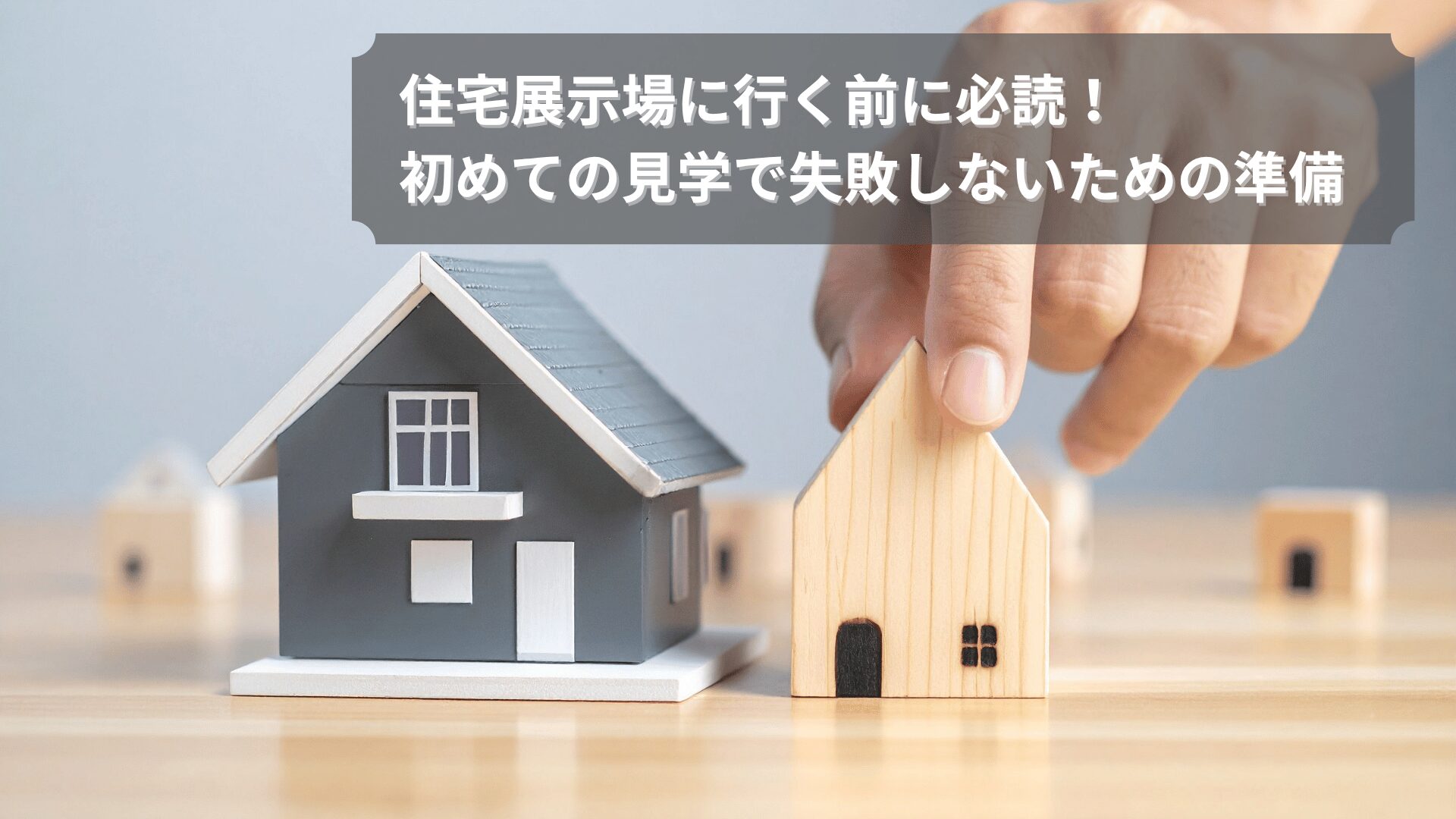 住宅展示場に行く前の準備をイメージした家の模型と人の手の写真。初めての見学で失敗しないためのポイントを表現。